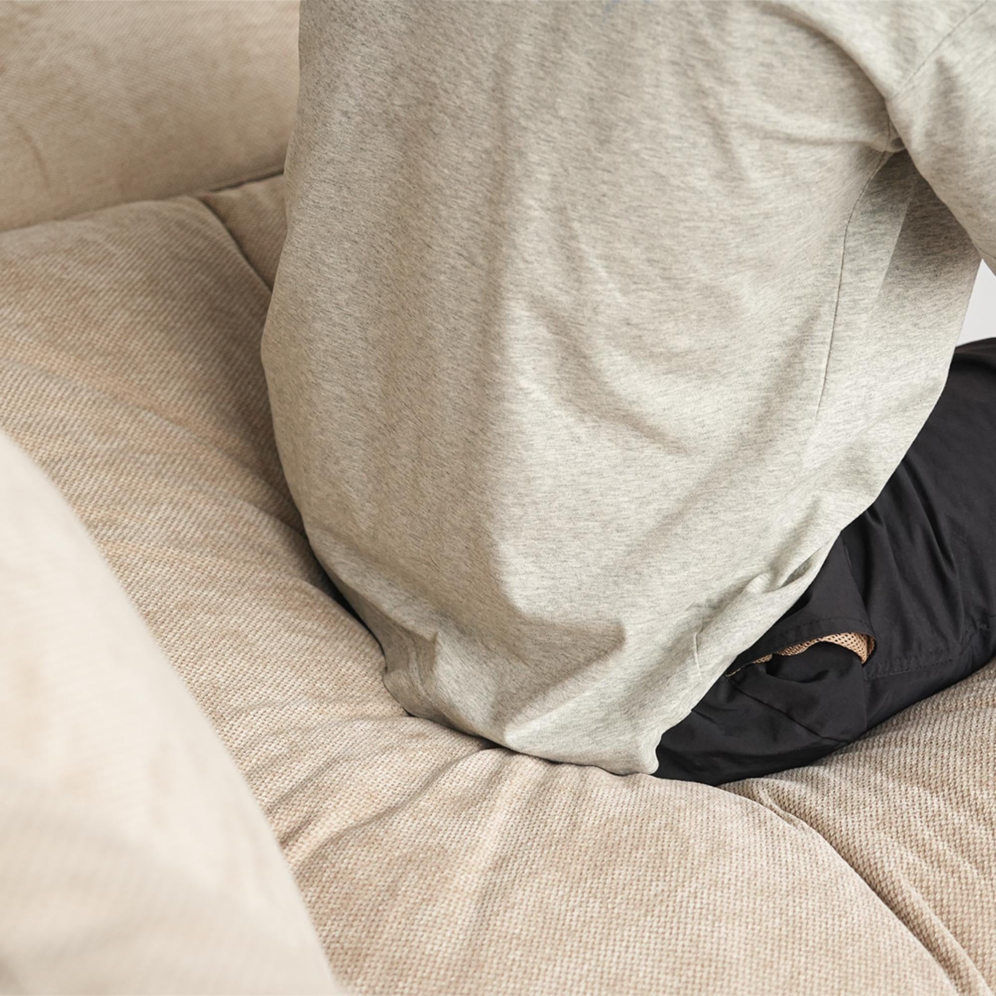 Person wearing a gray sweatshirt sitting on a beige couch