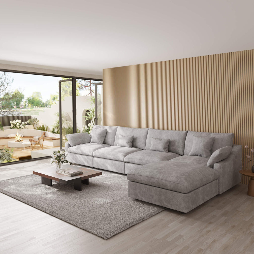 Light gray 5-seat sectional sofa with ottoman in a modern living room with large windows and a striped wall.