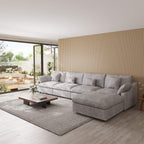 Light gray 5-seat sectional sofa with ottoman in a modern living room with large windows and a striped wall.