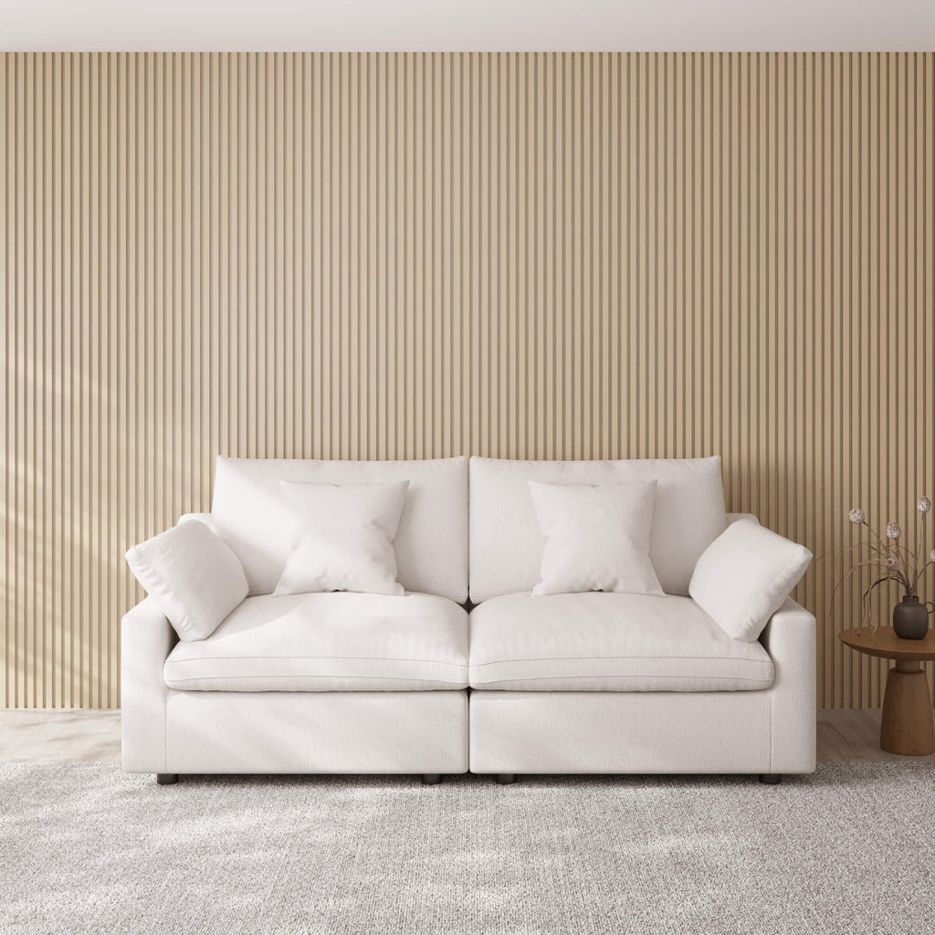 White loveseat sofa with decorative pillows against a beige paneled wall.