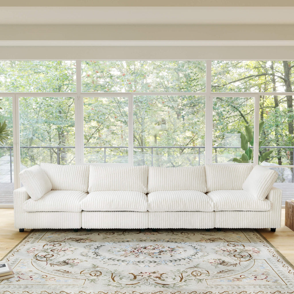 Beige faux rabbit fur 4-seat sofa in a room with large windows and a view of trees.