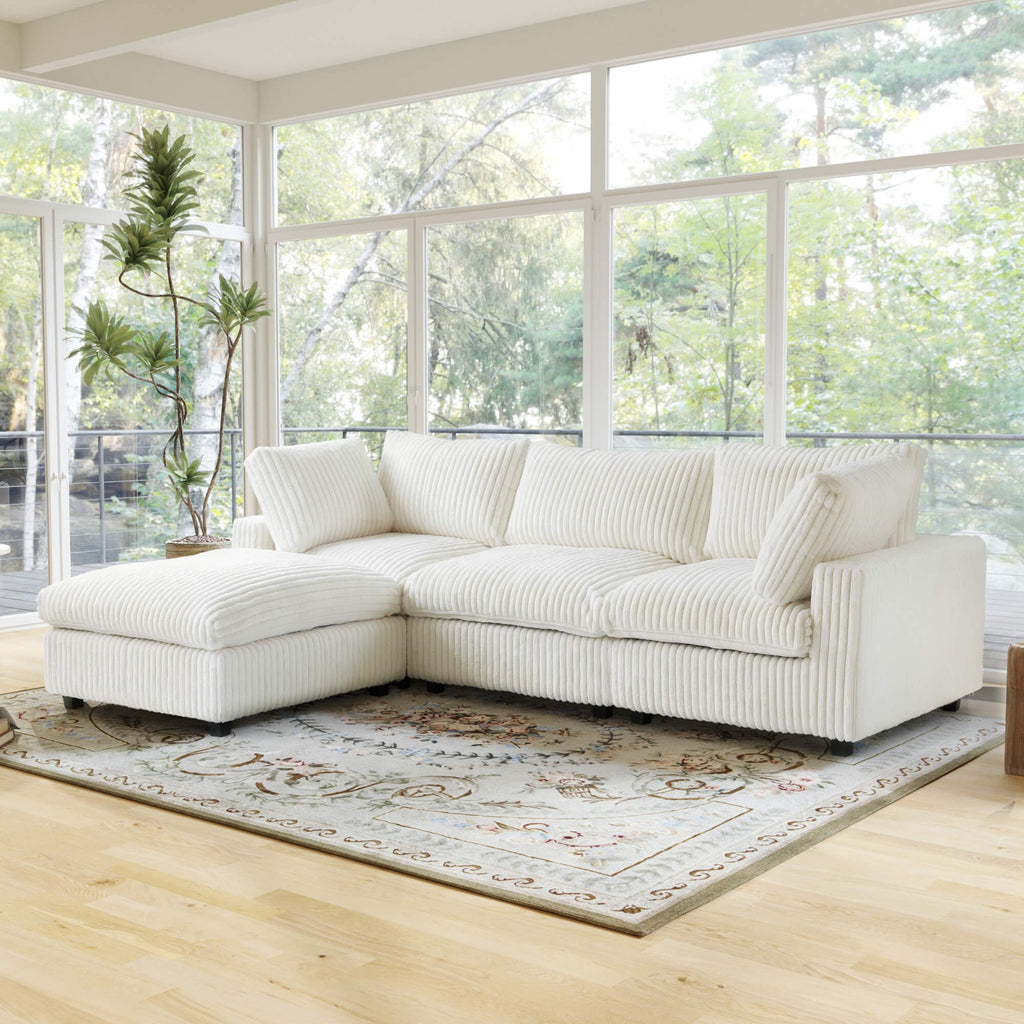 Beige L-shaped sectional sofa in a bright living room with large windows and plants.