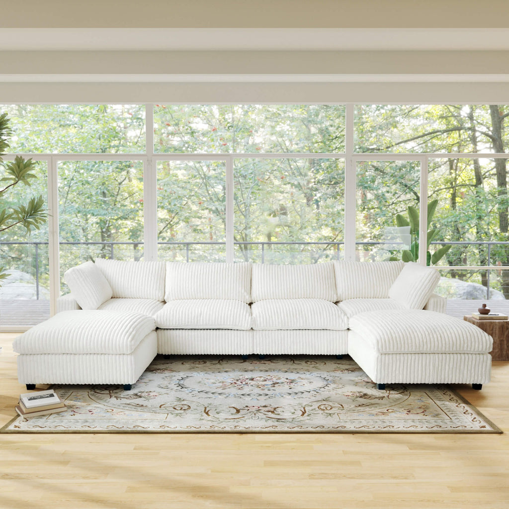 Beige U-shaped sectional sofa in a room with large windows and a view of trees.