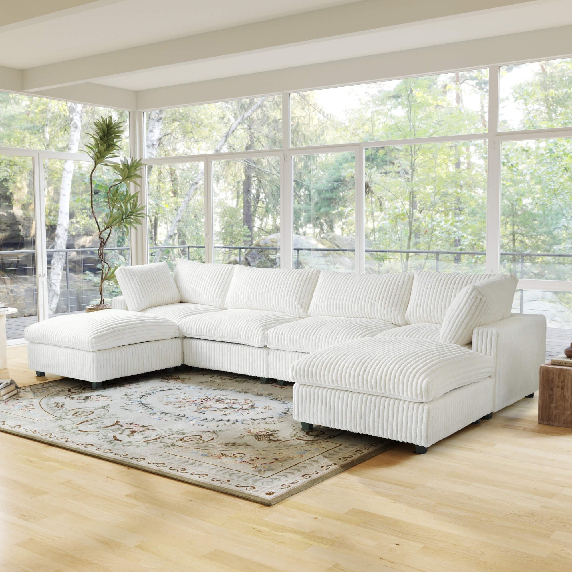 Beige U-shaped sectional sofa in a living room with large windows and a rug.