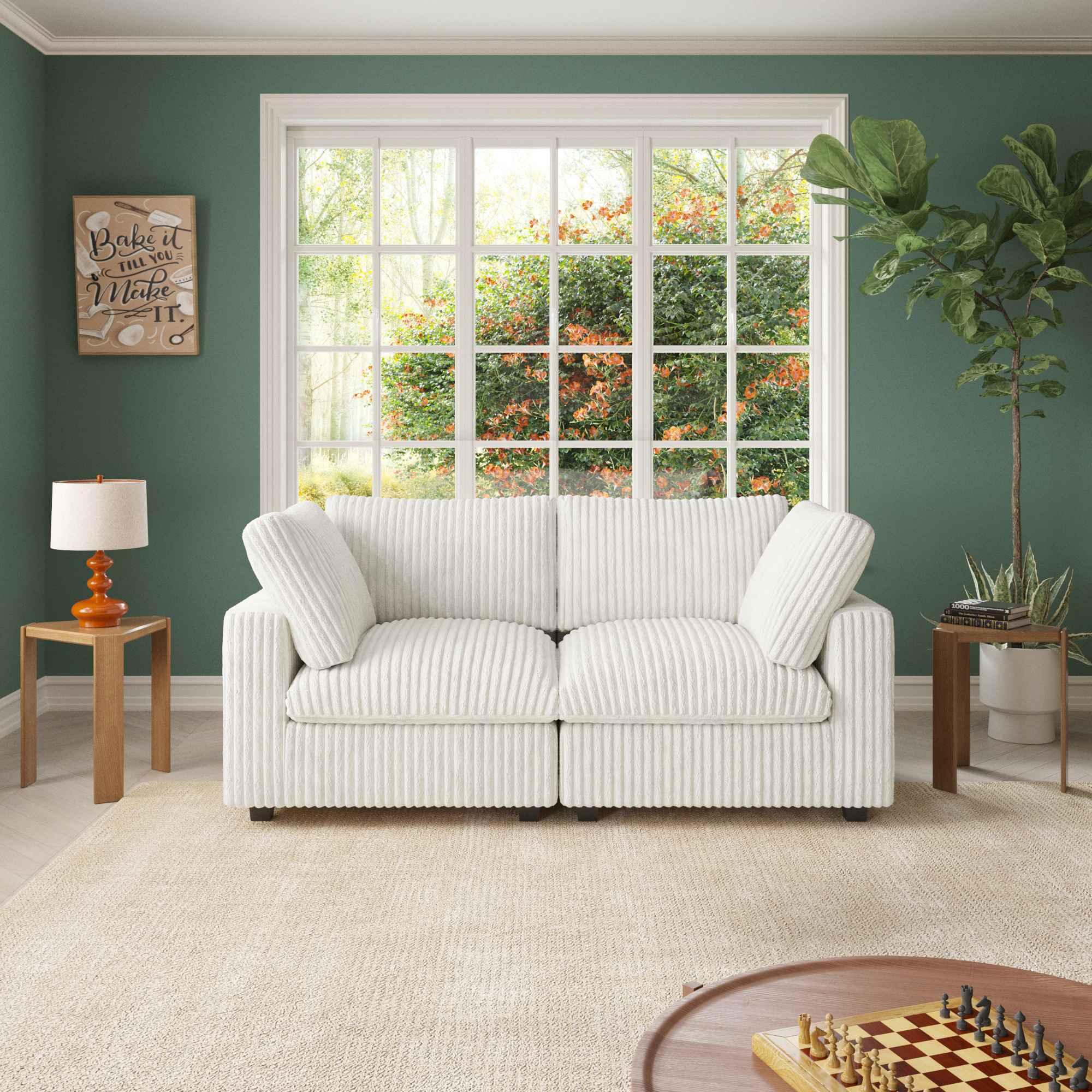A white faux rabbit fur 2-seater sofa with removable covers, positioned in a room with green walls, a large window, and a wooden floor.