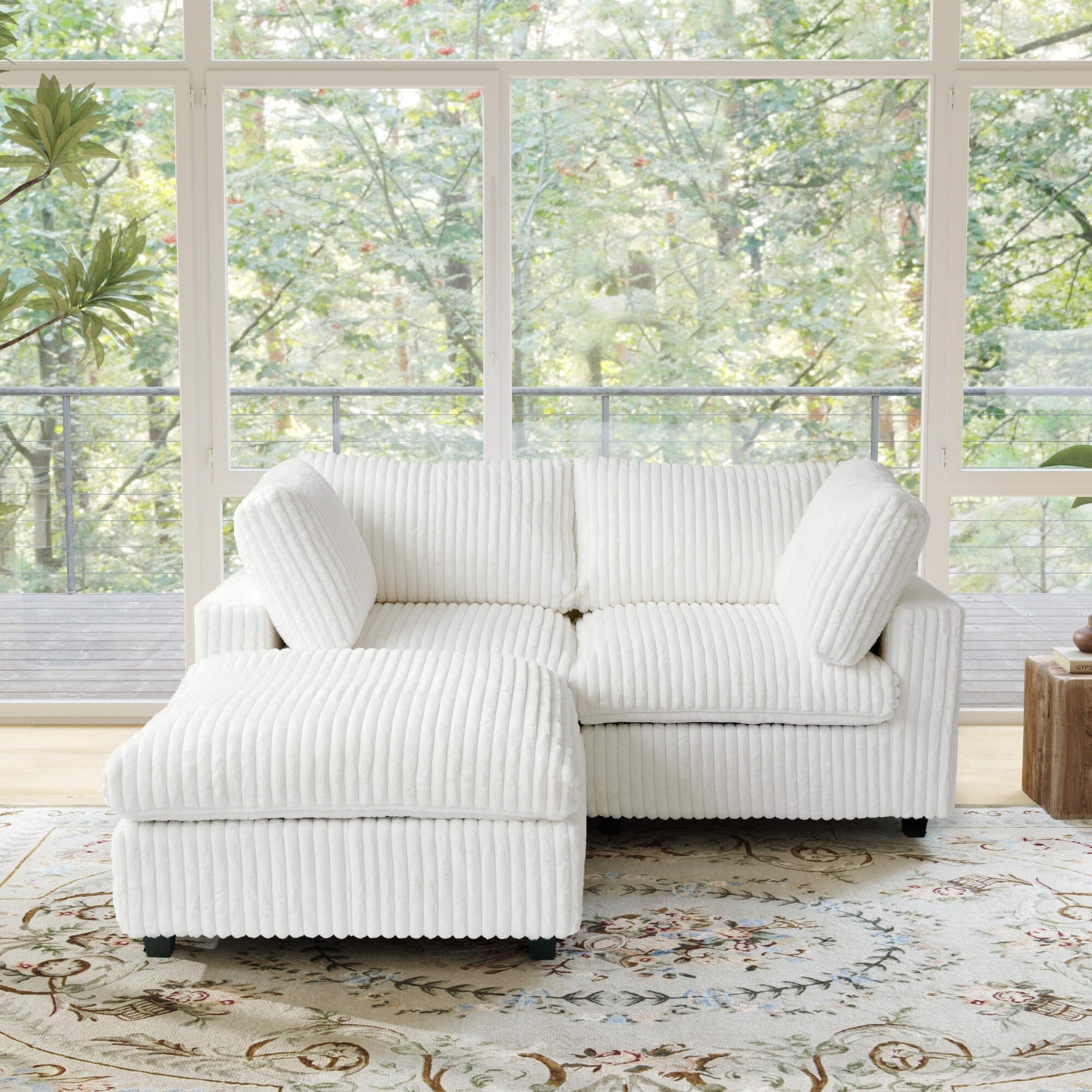 Beige faux rabbit fur sectional loveseat sofa with ottoman in a room with large windows and greenery outside.