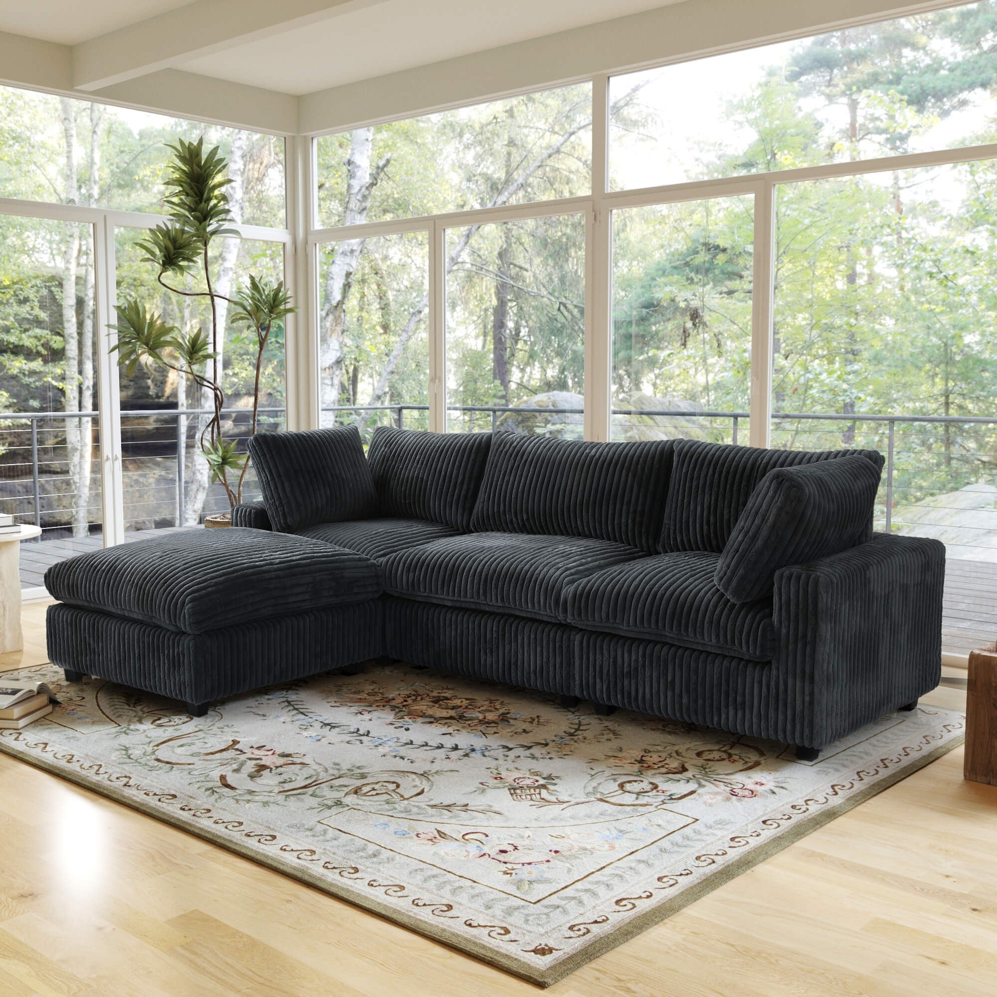 Black L-shaped sectional sofa in a living room with large windows and a decorative rug.