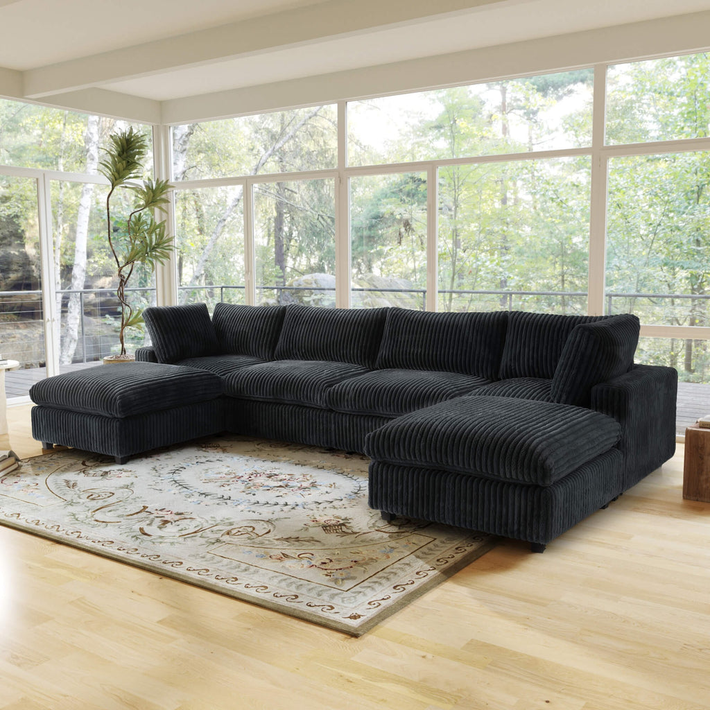 Black U-shaped sectional sofa in a living room with large windows and a rug.