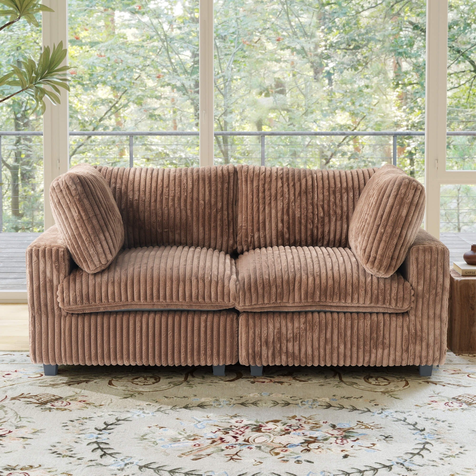 Brown faux rabbit fur sofa in a room with large windows and greenery outside.