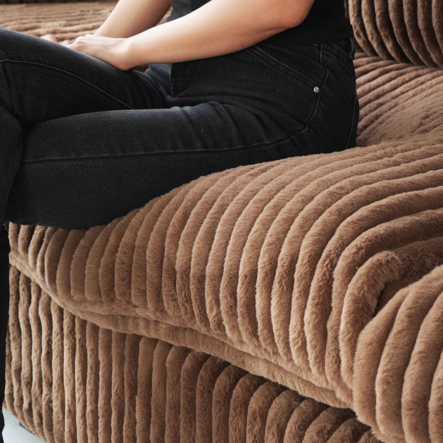 Person sitting on a seat cushion of a brown faux rabbit fur sofa