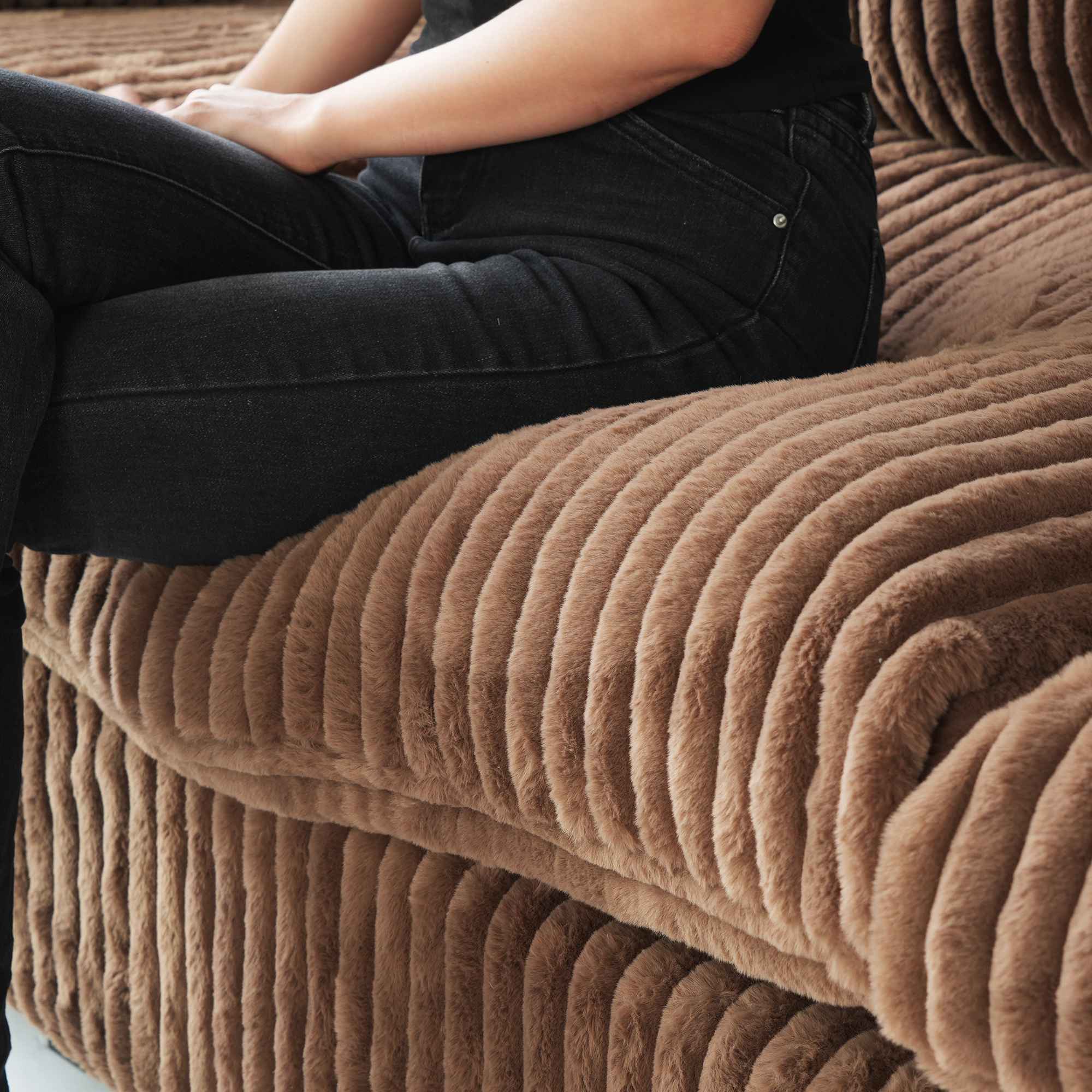 Person sitting on a seat cushion of a brown faux rabbit fur sofa