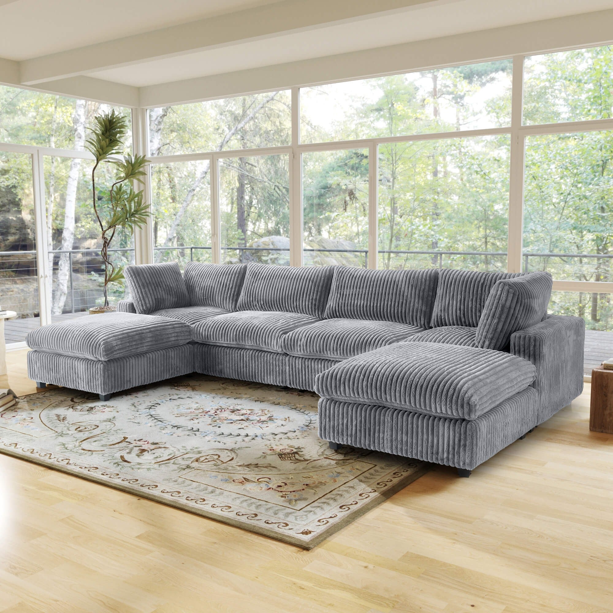 Gray U-shaped sectional sofa in a living room with large windows and a rug.
