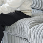Close-up of a person sitting on a seat cushion of a faux rabbit fur sofa in light gray