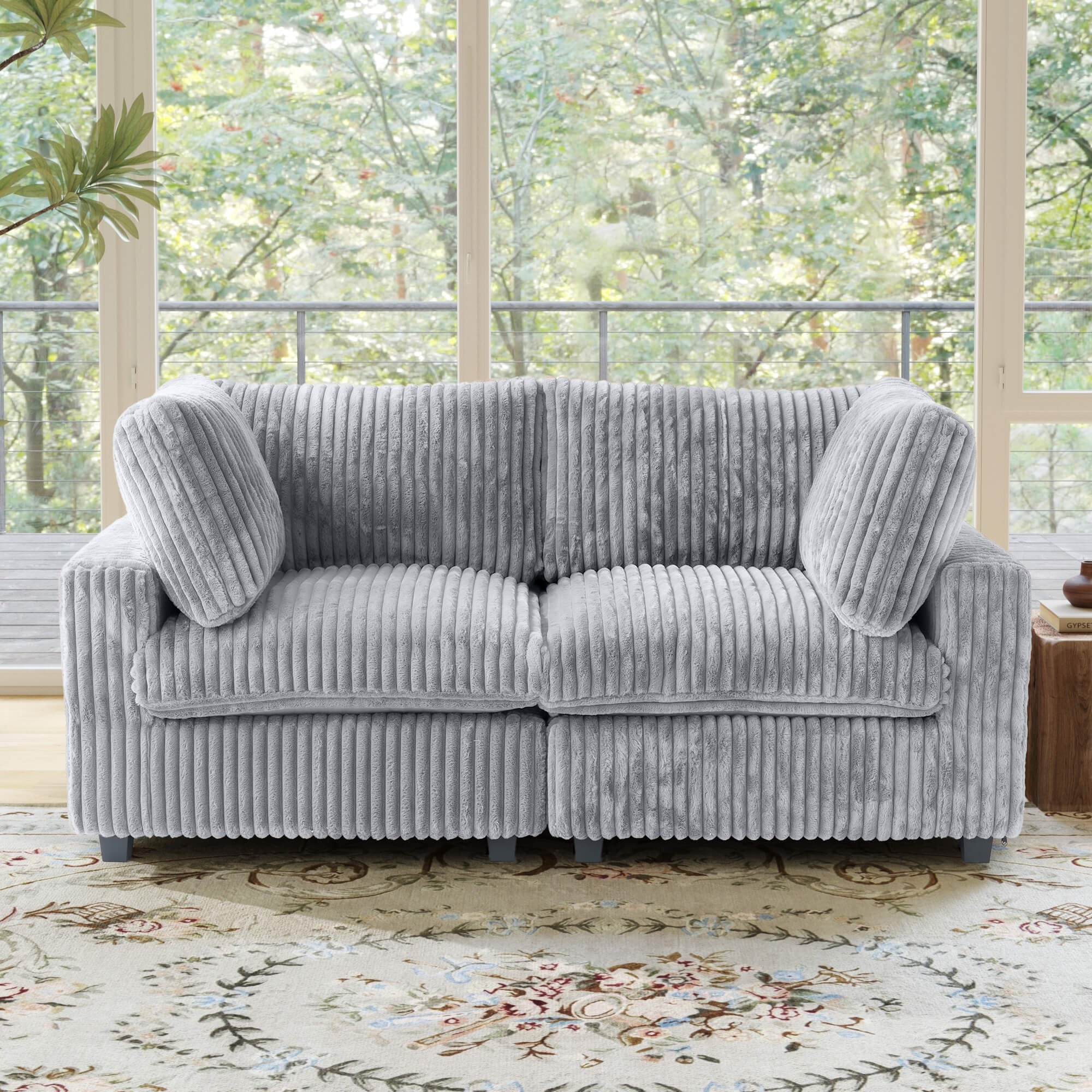 Light gray faux rabbit fur loveseat sofa with fluffy cushions in a room with large windows and greenery outside
