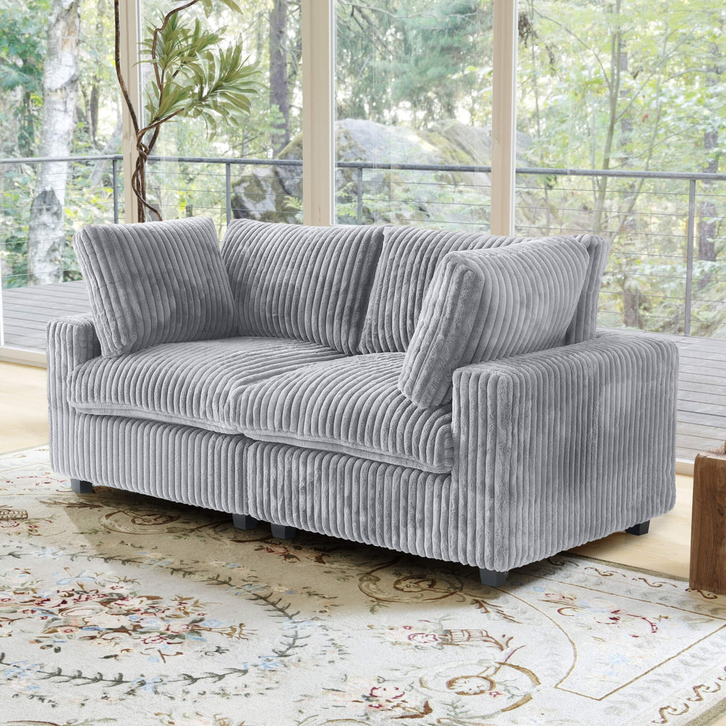 Gray loveseat sofa in a living room with large windows and a decorative rug.