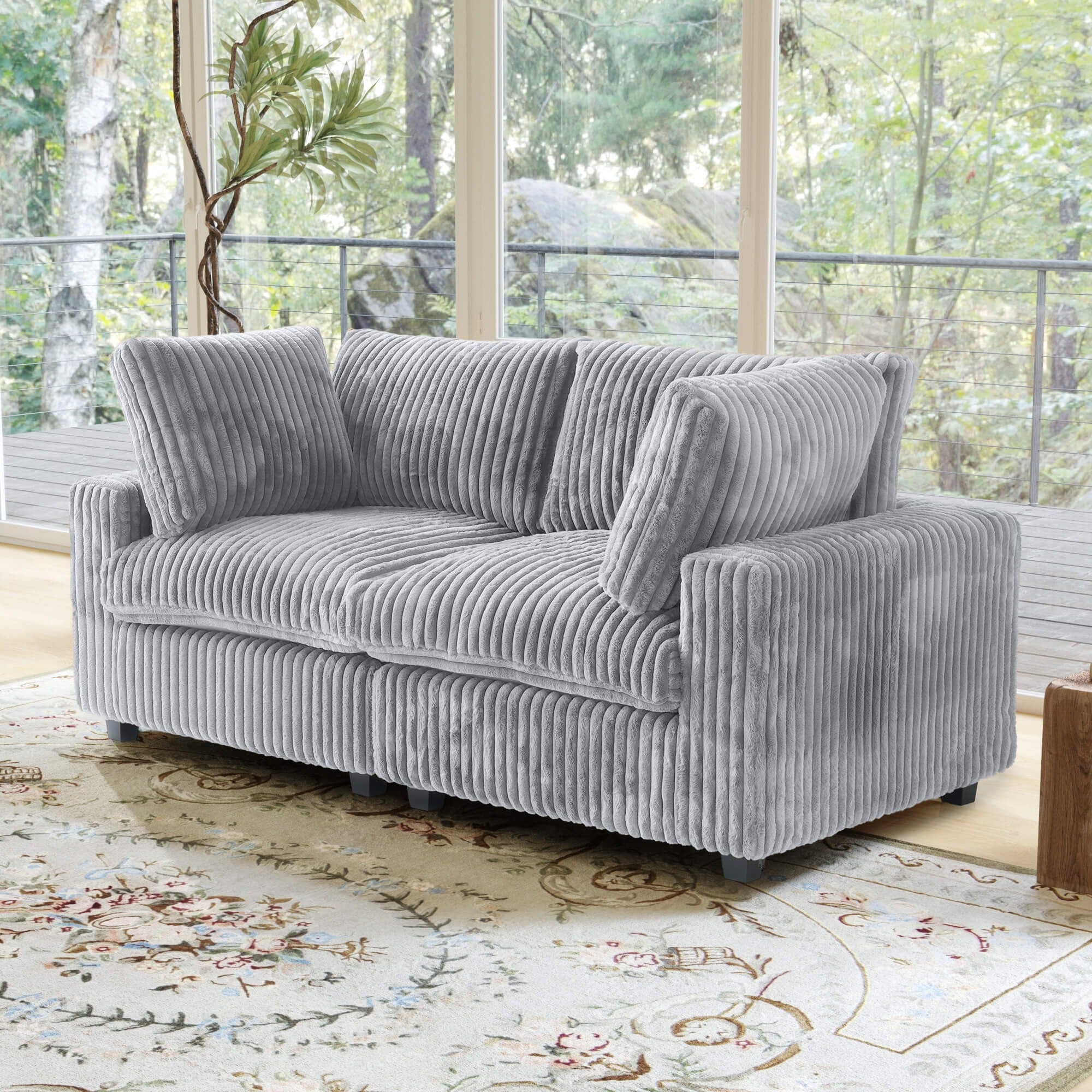 Gray loveseat sofa in a living room with large windows and a decorative rug.