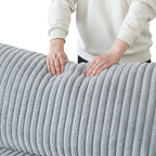 Person holding a faux rabbit fur gray backrest cushion of a sofa with a white background