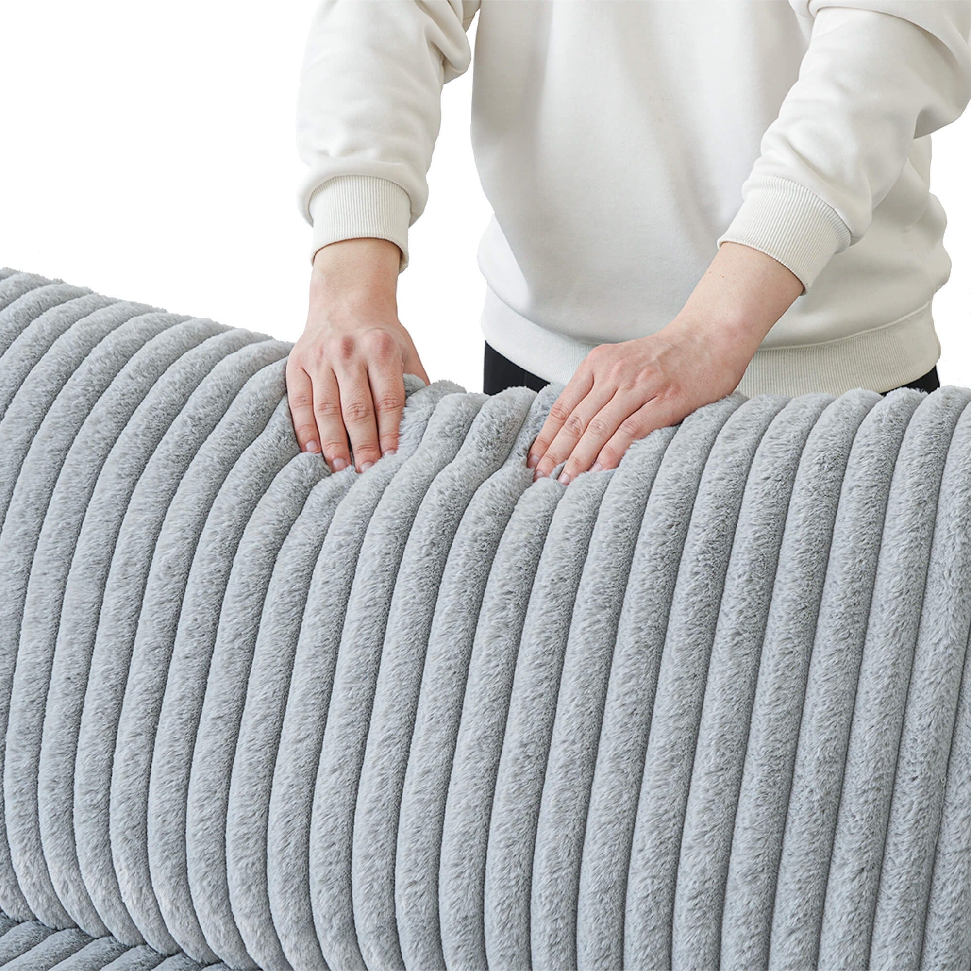 Person holding a faux rabbit fur gray backrest cushion of a sofa with a white background