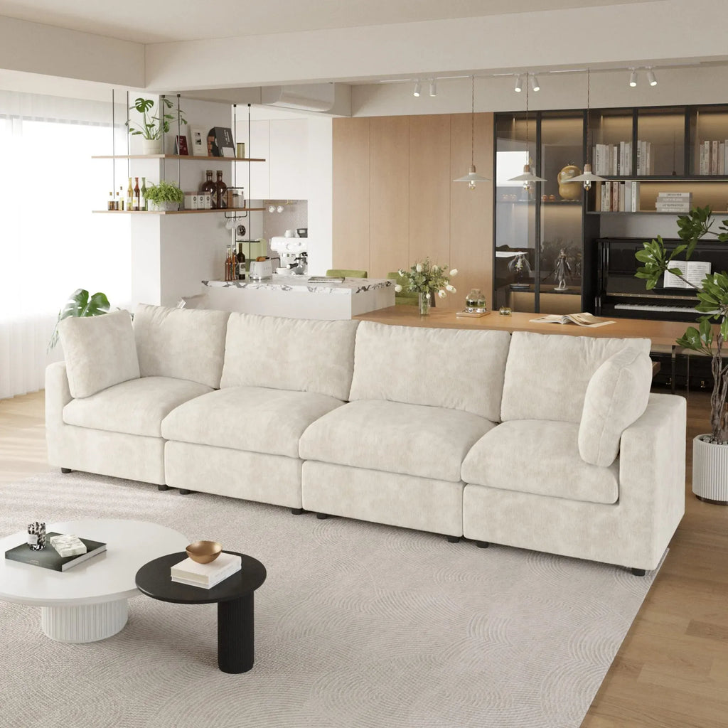 Modern living room with a beige 4-seater sofa, coffee table, and kitchen in the background.