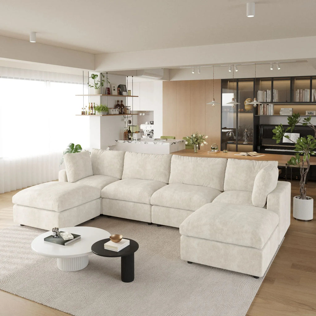 Modern living room with a beige U-shaped 6-seater sectional sofa, coffee table, and kitchen in the background.