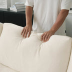 Person adjusting a beige back cushion on a sofa