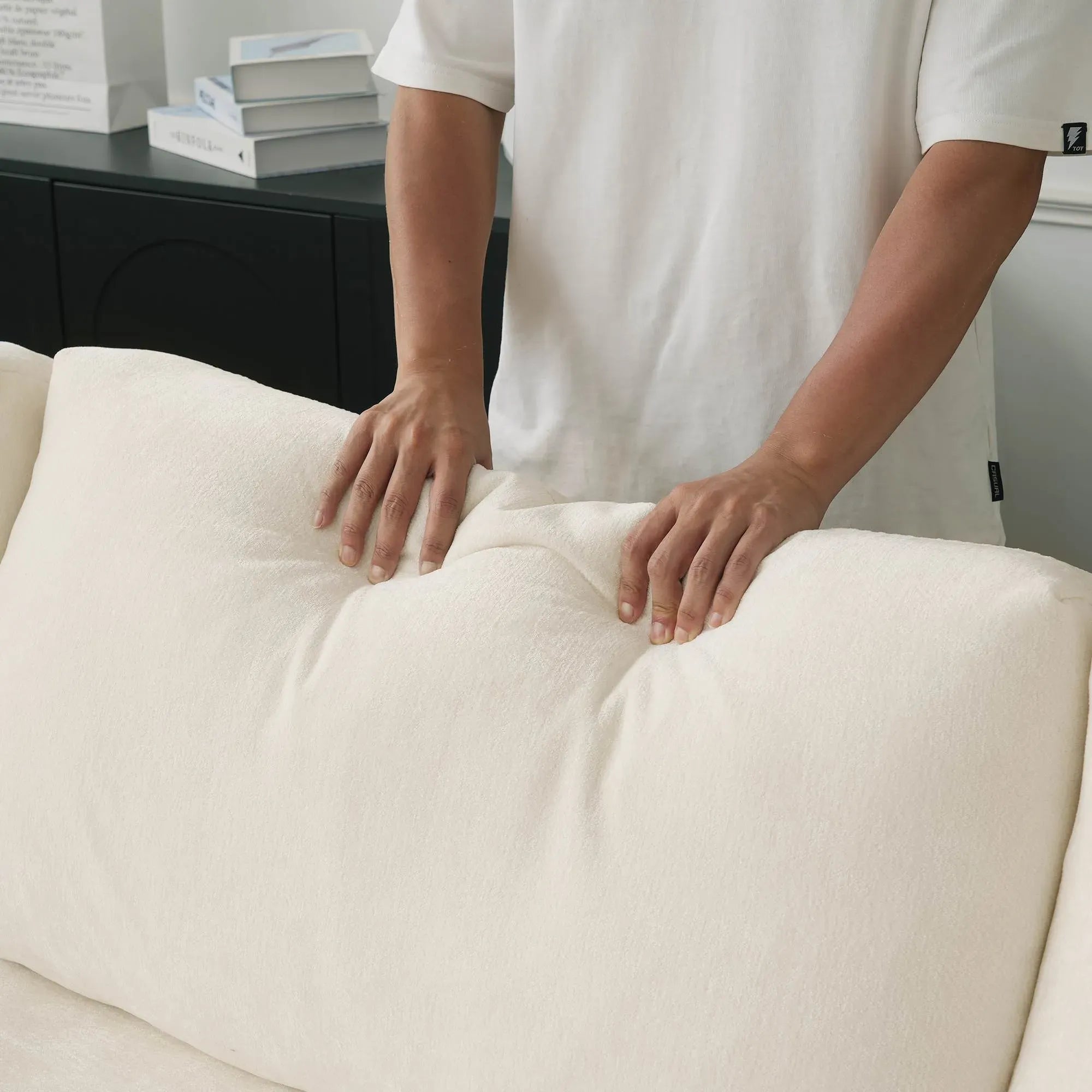 Person adjusting a beige back cushion on a sofa