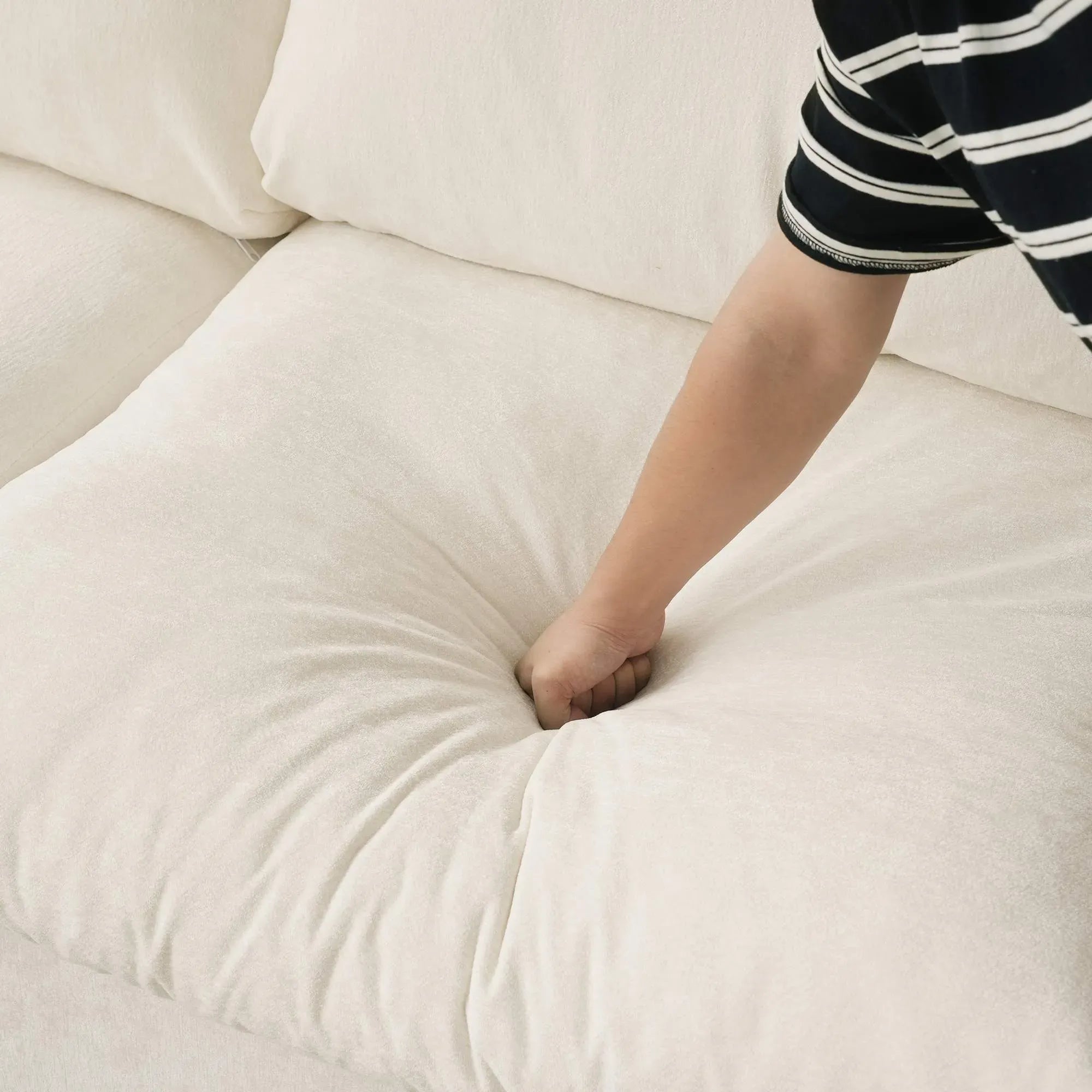 Person pressing on a seat cushion of a beige sofa