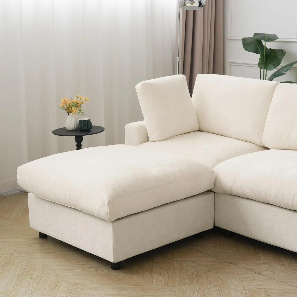 Beige sectional sofa in a living room setting with a small table and plant.