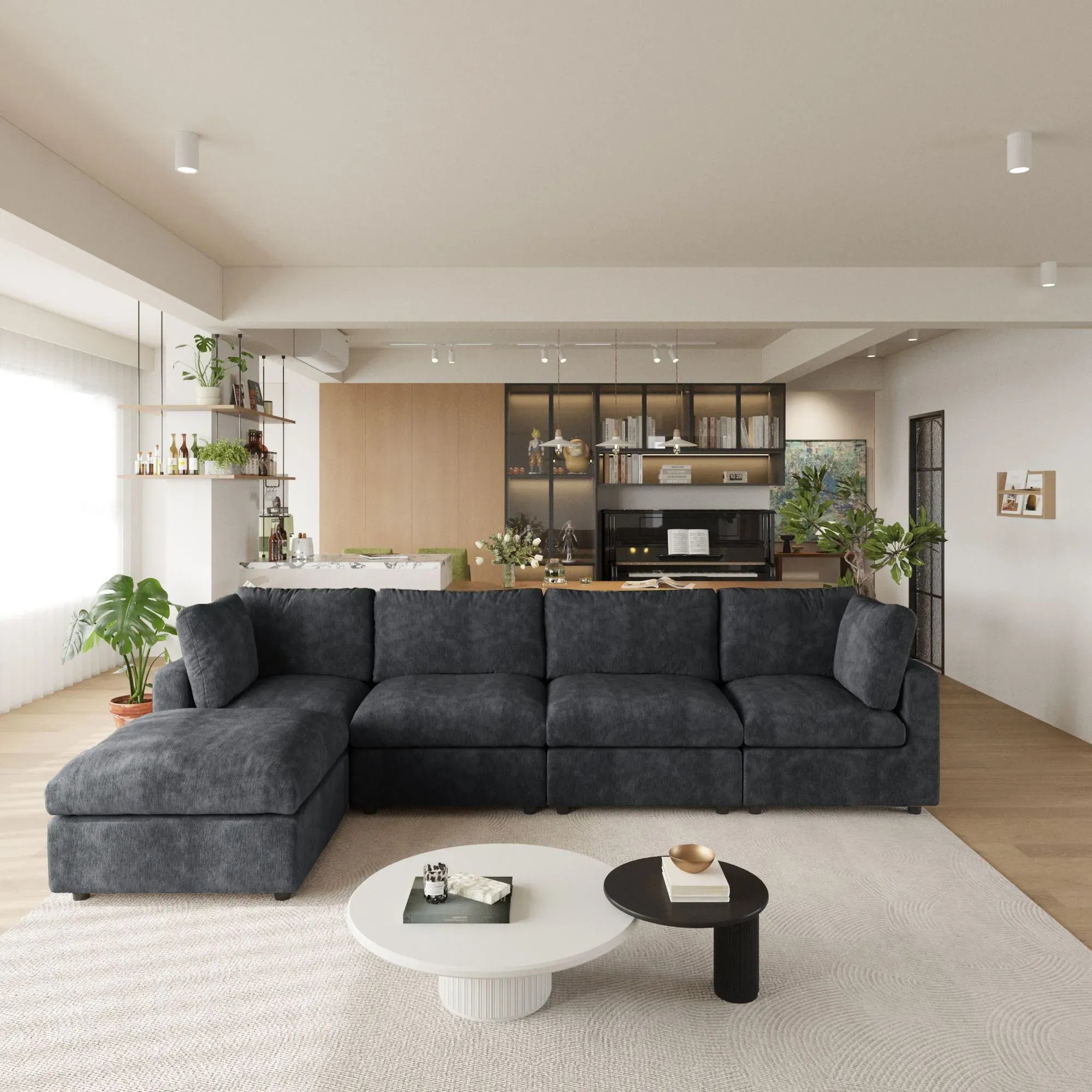 Modern living room with a black L-shaped 5-seater sectional sofa, coffee tables, and a kitchen in the background.