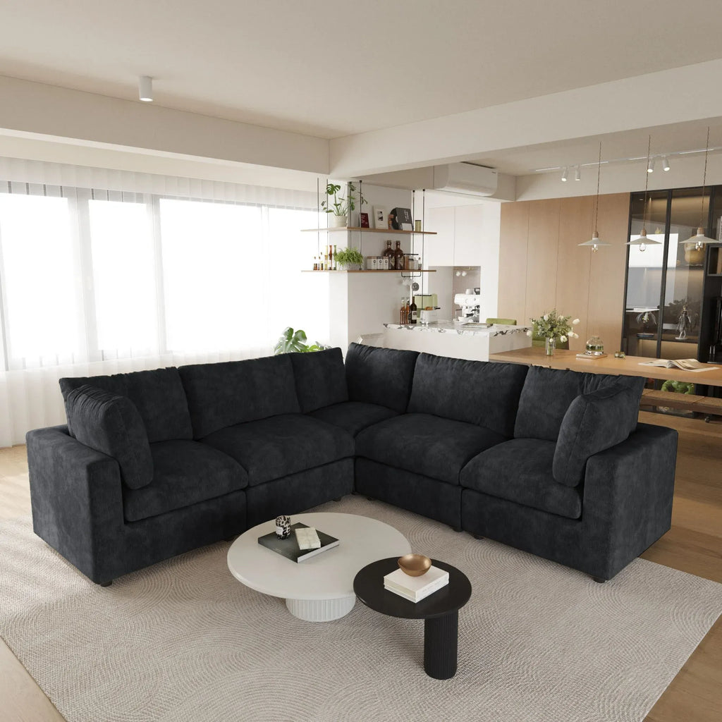 Modern living room with a black 5-seater corner sectional sofa, coffee table, and kitchen in the background.