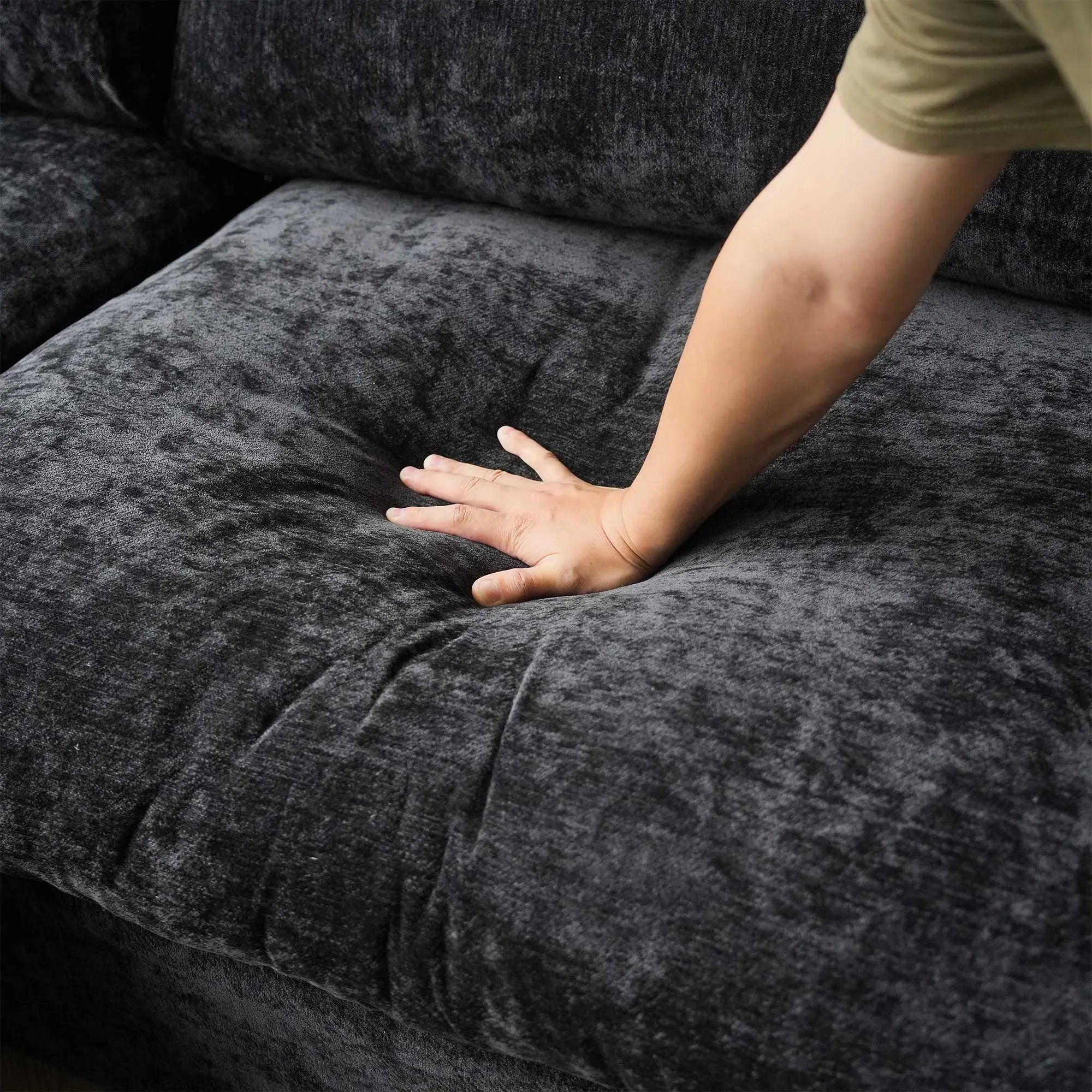 Person's hand touching a black textured sofa