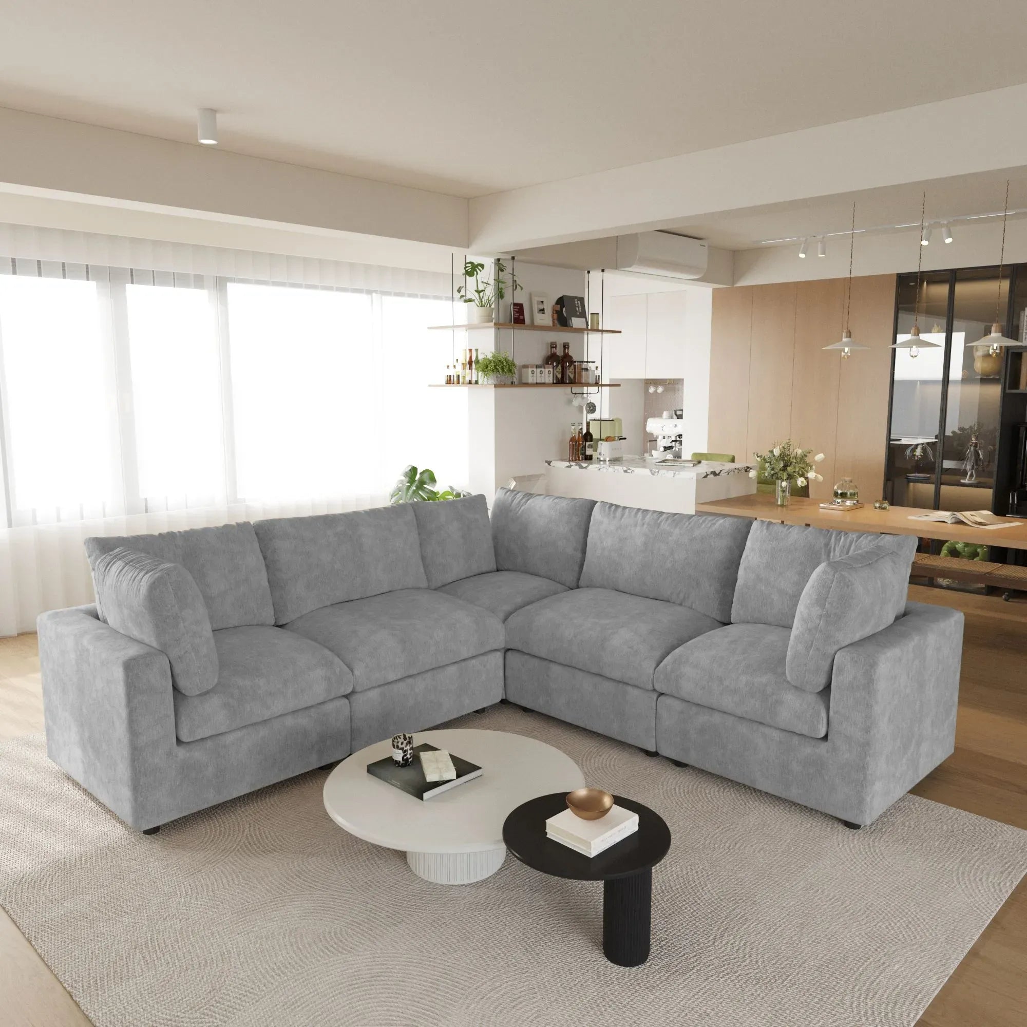 Gray 5-seater corner sectional sofa in a modern living room with a kitchen in the background.