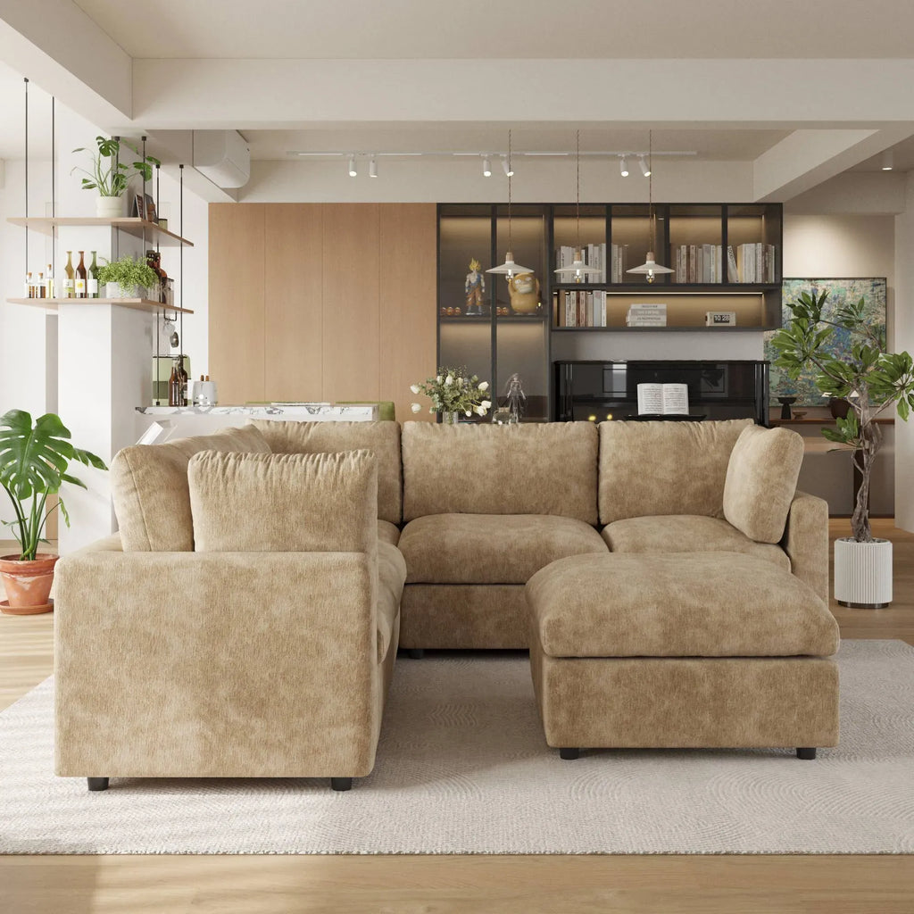 Khaki V-shaped corner sectional sofa with ottoman in a modern living room with decor elements.