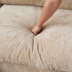 Close-up of a hand pressing onto seat cushion of a khaki colored sofa