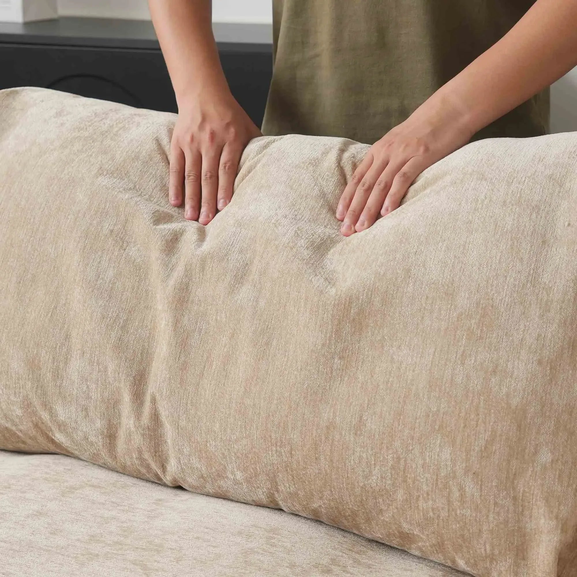 Person squishing a back cushion of a khaki sofa to show its softness